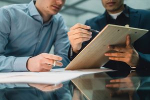 Zwei Männer sitzen vor einem Klemmbrett und machen Notizen.