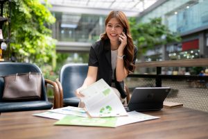 Eine Frau im Büro telefoniert und blättert in weiß-grünen Papieren. Hinter ihr sind viele Pflanzen.