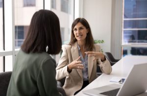 Zwei Frauen sitzen an einem Verhandlungstisch und besprechen etwas.